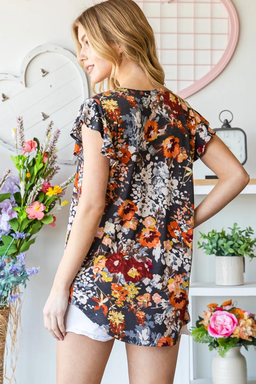 Heimish full size floral ruffled round neck cap sleeve blouse with ruffle details and floral pattern, displayed on a hanger.
